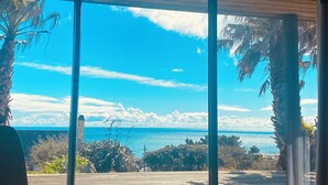 Ein Zimmer mit großen Schiebeglasfenstern, die auf eine Terrasse mit Meer- und Palmenblick führen.