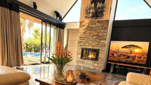 Ein geräumiges Wohnzimmer mit Ledersofas, einem Kamin und einem großen Fernseher, der eine Savannenszene zeigt.