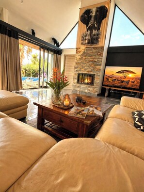 Ein geräumiges Wohnzimmer mit Ledersofas, einem Kamin und einem großen Fernseher, der eine Savannenszene zeigt.