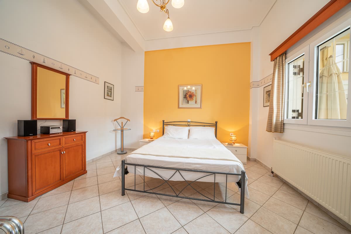 A bedroom with a bed, wooden dresser, bedside lamps, and a window with curtains.