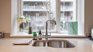 A modern kitchen with a stainless steel sink, a window with a view of a building, and a vase with flowers on the windowsill. - Stunning Townhouse XII - Cosy but spacious home from home stays, all in one. (London)