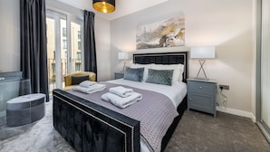 A modern bedroom with a large bed, bedside lamps, a nightstand, a round ottoman, and a view of the outside. - Stunning Townhouse XII - Cosy but spacious home from home stays, all in one. (London)