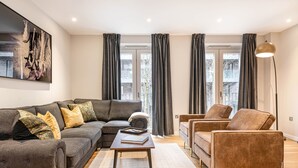A modern living room with a grey sofa, a brown armchair, and a coffee table. - Stunning Townhouse XII - Cosy but spacious home from home stays, all in one. (London)