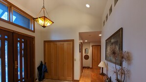 Un pasillo con una puerta de madera, un colgador de luz, una alfombra y una mesa con objetos decorativos.
