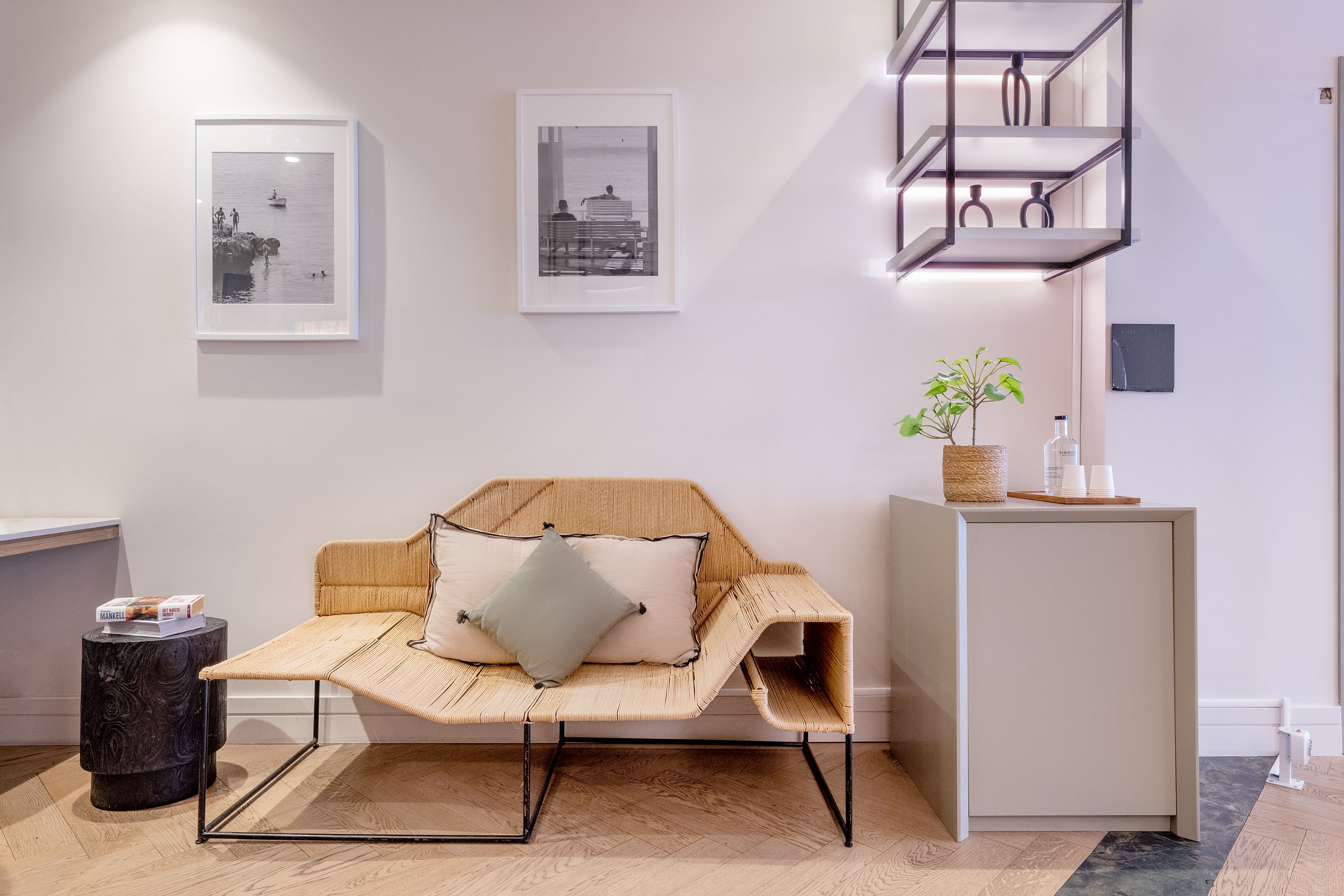 A room with a rattan sofa, a small round table, and a minimalist shelving unit.