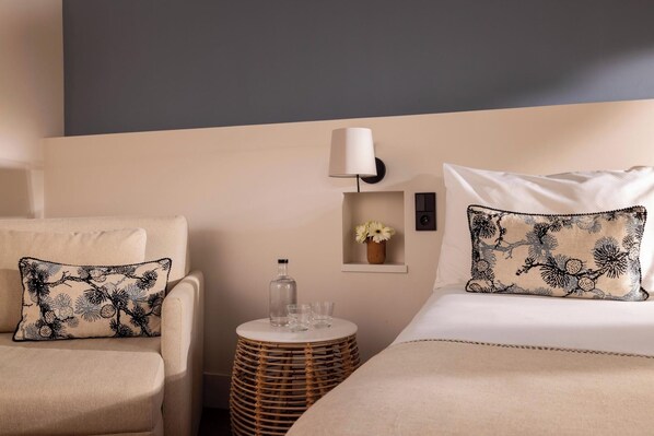 A hotel room with two beds, a nightstand, a lamp, and a small table with glasses.