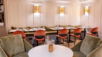 Een restaurant met ronde tafels, zachte zitplaatsen en wandlampen.