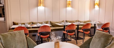 A restaurant with round tables, cushioned seating, and wall-mounted lighting.