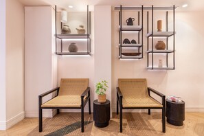 A room with two wicker chairs, a small table with a plant, and a wall-mounted shelf with decorative items. - Crisol Mozart (Nice)
