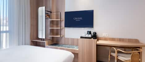 A hotel room with a bed, a desk, a chair, a TV, and a wardrobe.