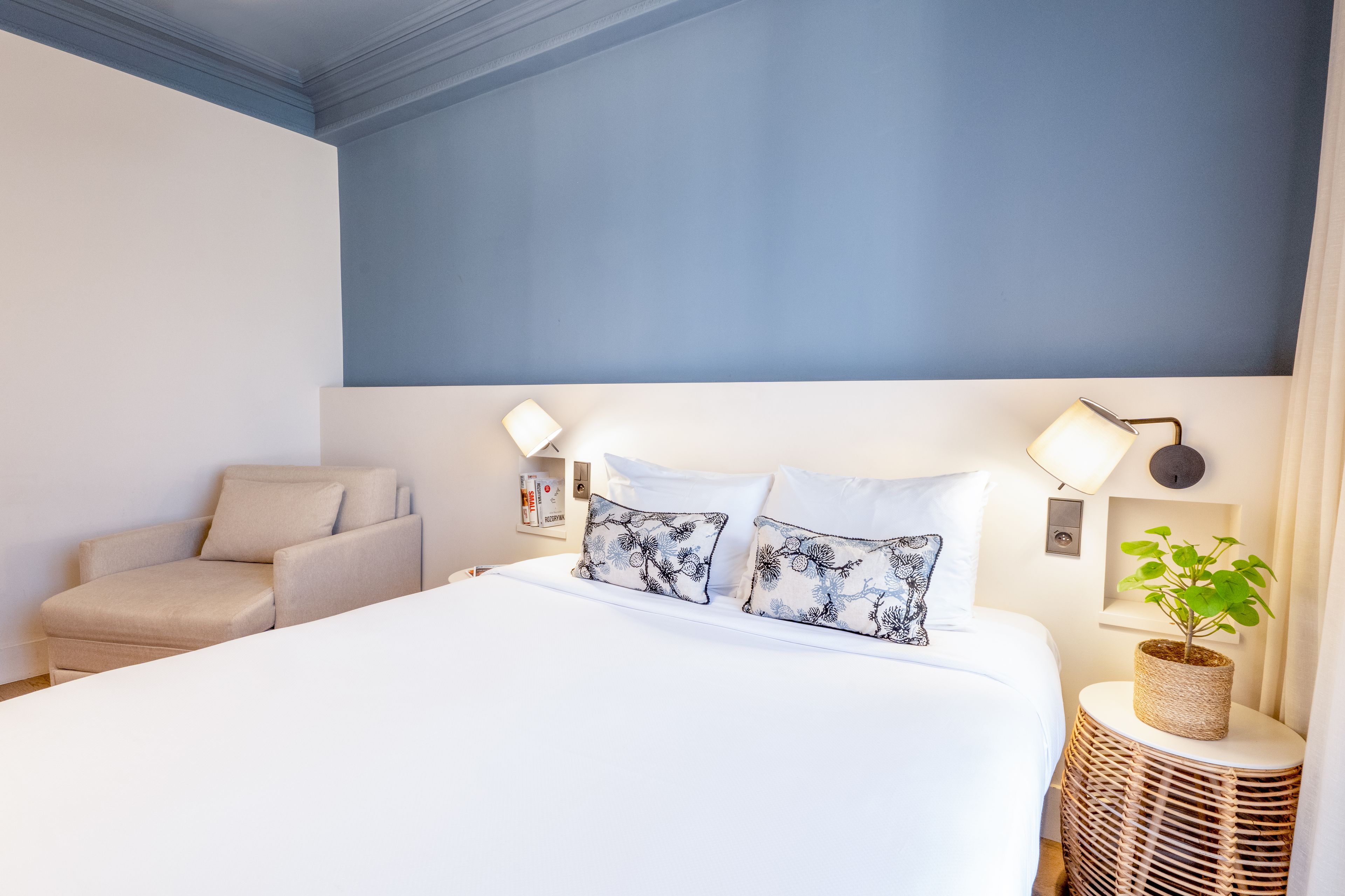 Quarto de hotel com cama, cadeira, abajur e uma pequena planta.