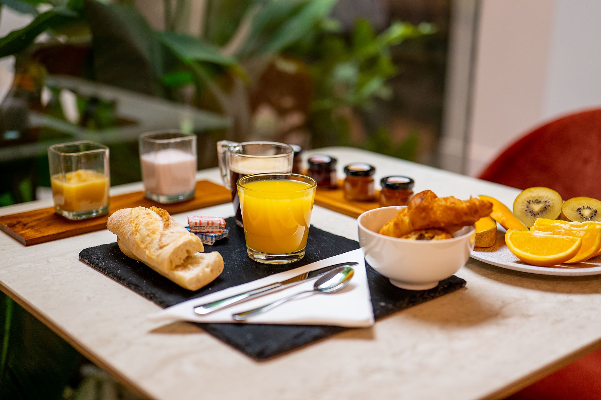 A breakfast setting with croissants, orange juice, and a bowl of fruit on a table.