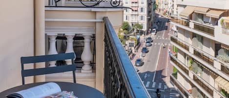 A balcony with a table and chairs, overlooking a street with buildings and a distant mountain.