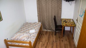 A small room with a wooden bed, a chair, and a small table with a patterned tablecloth.