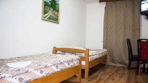 Uma cama de solteiro com colcha estampada, cabeceira de madeira, uma mesinha, uma cadeira, televisão em suporte e um quadro na parede.