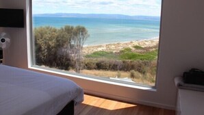 A bedroom with a large window offering a view of a beach and ocean. - Three Little Birds at Freycinet - Ocean views! (Glamorgan-Spring Bay)