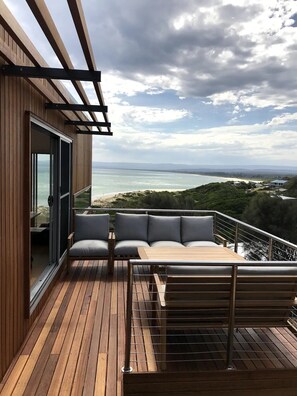 A wooden deck with a sofa and table, overlooking a beach and ocean.