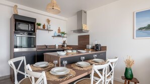 Une cuisine moderne avec un coin repas, comprenant un four encastré, un four à micro-ondes et une table à manger en bois pour quatre personnes.