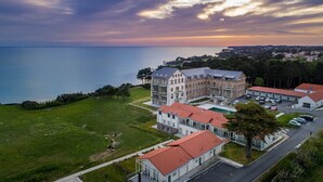 Un grand bâtiment à plusieurs étages, doté d’une cour intérieure, entouré d’une zone verdoyante et bordé par un plan d’eau.
