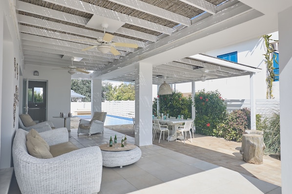 A covered outdoor seating area with wicker furniture, a pool, and a dining table.