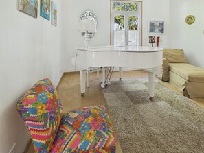 Une pièce avec un piano blanc, un canapé beige, un pouf coloré à motifs et un tapis.