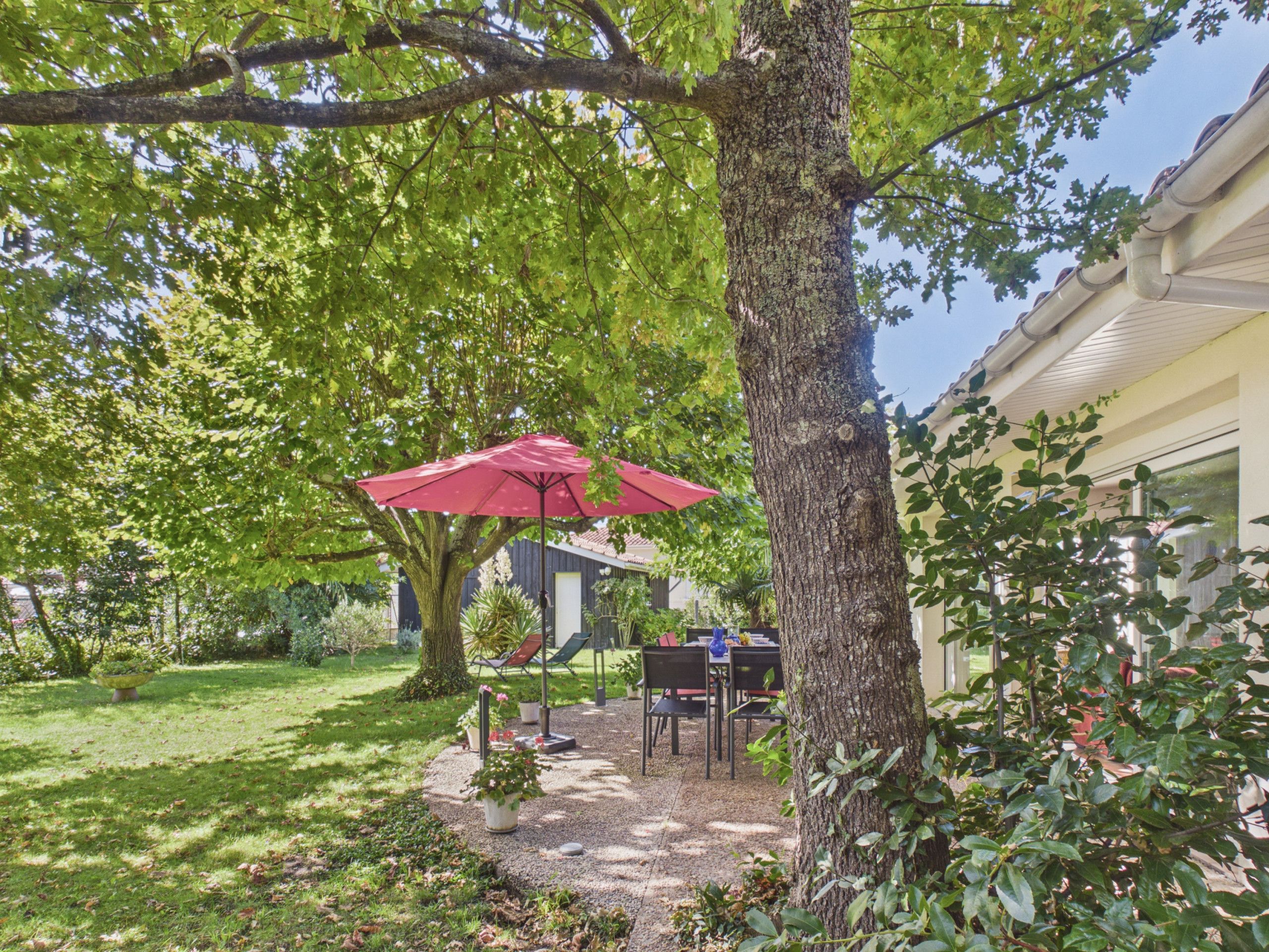 A patio with a table and chairs, surrounded by trees and a red umbrella.