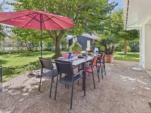 An outdoor patio with a table and chairs, a red umbrella, and a potted plant. - 200m from the beach- House with great garden (Andernos-les-Bains)