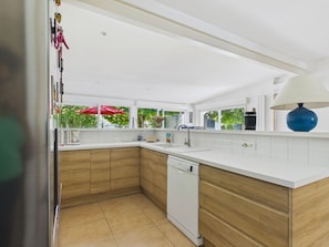 A modern kitchen with white countertops, wooden cabinets, a dishwasher, and a window with a red umbrella. - 200m from the beach- House with great garden (Andernos-les-Bains)