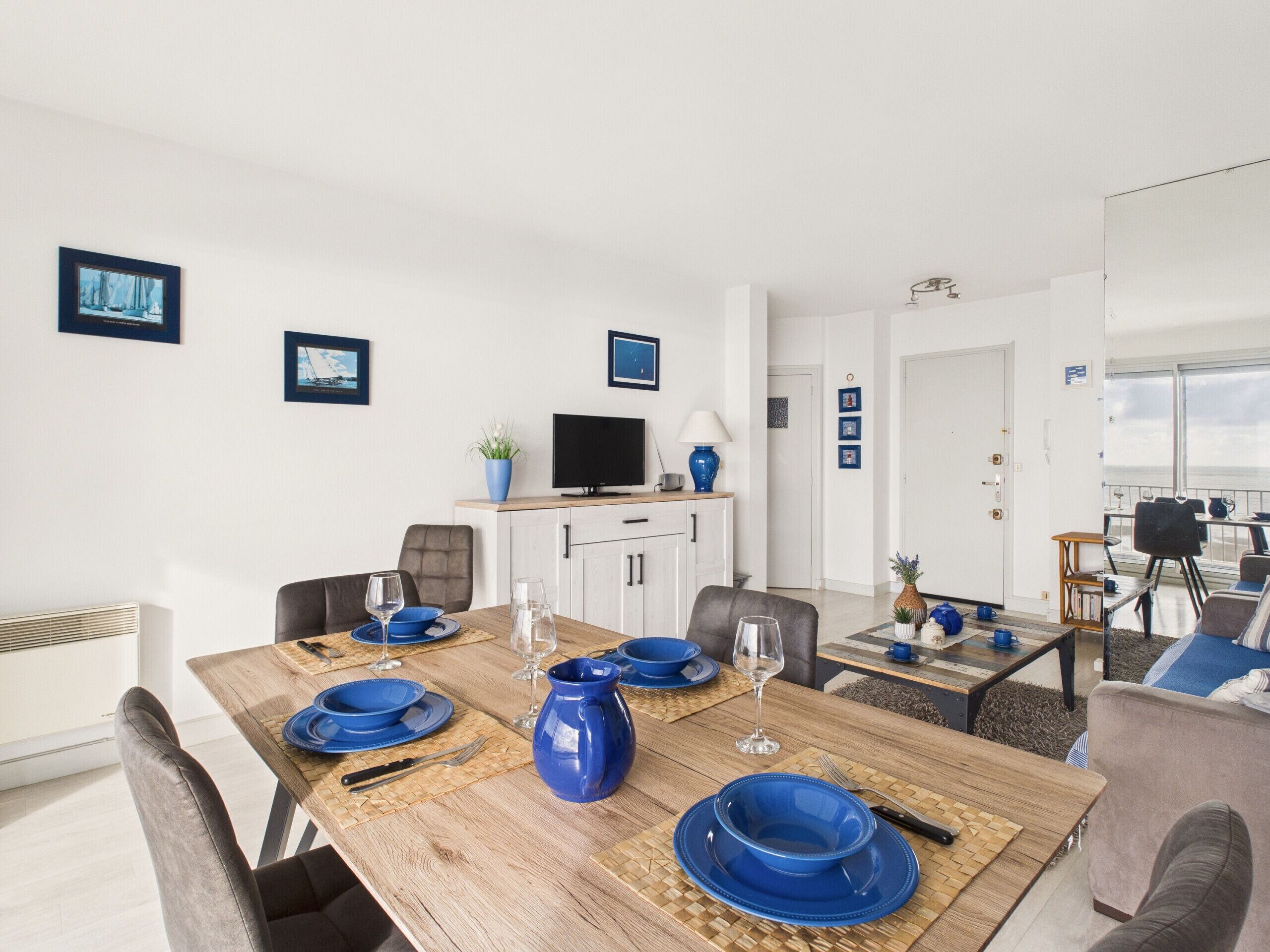 Una sala moderna con una mesa de comedor de madera preparada para cuatro personas, un televisor y un sofá.