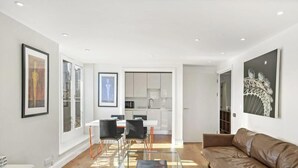 A modern living room with a brown leather sofa, a glass coffee table, and a dining area with a white table and black chairs.