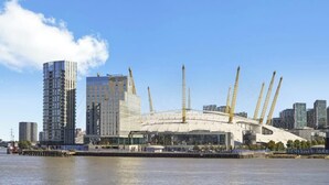 A waterfront view of a modern stadium with multiple cranes, surrounded by high-rise buildings.