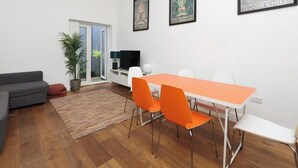 Un salon moderne avec un canapé gris, des fauteuils orange, une table blanche et un téléviseur.