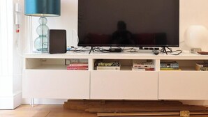 Un téléviseur à écran plat posé sur un meuble blanc, avec une lampe et des livres à proximité.