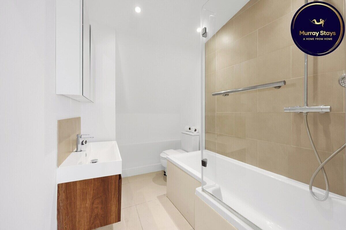 Een moderne badkamer met een douchecabine van glas, een witte wastafel en een toilet.