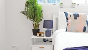 Une chambre à coucher avec un lit, une table de chevet, une lampe et une plante en pot.