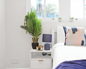 Une chambre à coucher avec un lit, une table de chevet, une lampe et une plante en pot.