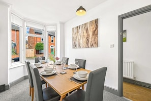 A dining room with a wooden table set for six, large windows, and a view of a brick building outside.