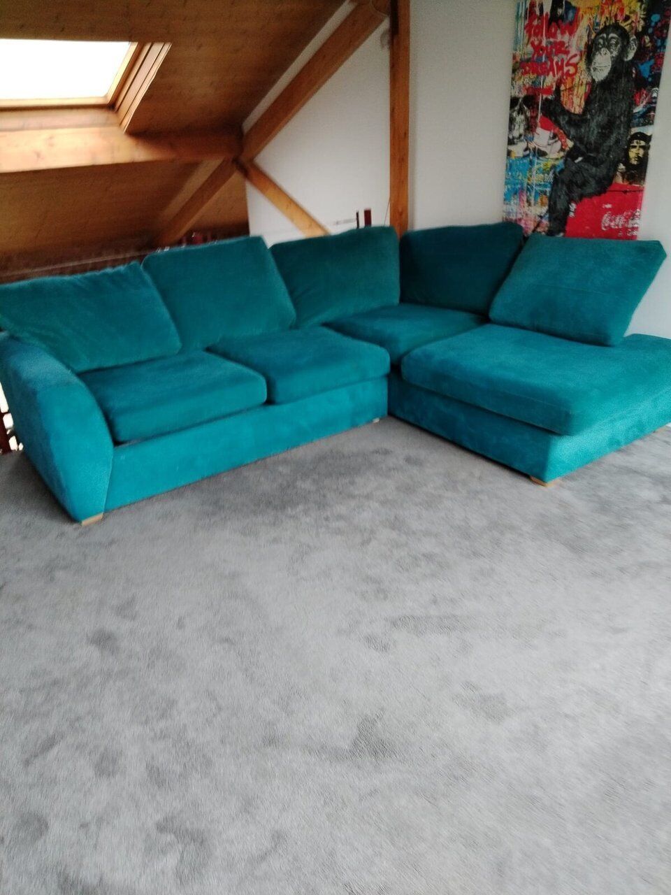 A teal sectional sofa in a room with a sloped ceiling and a colorful abstract painting on the wall.