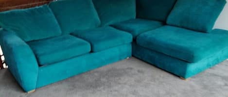 Un sofá seccional color turquesa en una habitación con techo inclinado y un cuadro abstracto colorido en la pared.