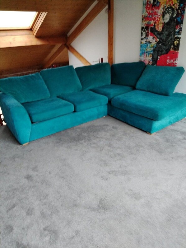 A teal sectional sofa in a room with a sloped ceiling and a colorful abstract painting on the wall.