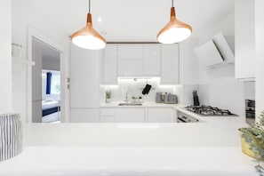 A modern kitchen with white cabinets, a gas stove, a toaster, and pendant lighting.