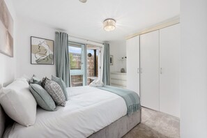 A bedroom with a bed, pillows, a nightstand, a wardrobe, and a window with curtains.