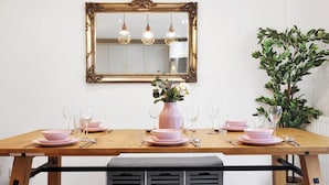 A dining table set with pink dishes and glasses, a mirror above, and a plant to the right.