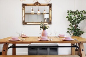 A dining table set with pink dishes and glasses, a mirror above, and a plant to the right.
