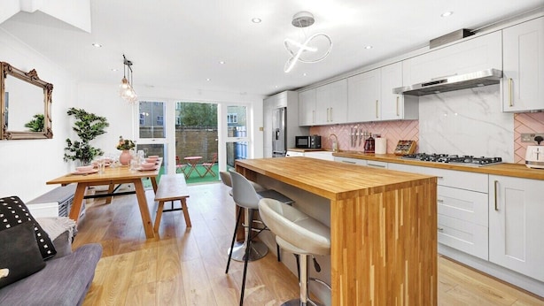 A modern kitchen with white cabinets, a wooden island, and a dining area with a table and chairs.