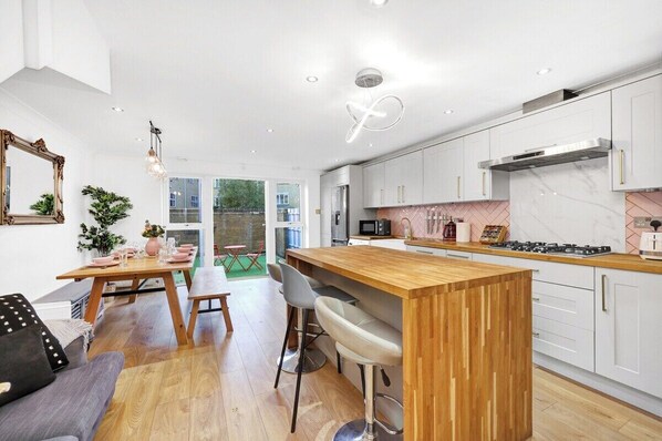 A modern kitchen with white cabinets, a wooden island, and a dining area with a table and chairs.