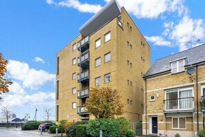 A multi-story residential building with balconies, a parking area, and a clear sky.