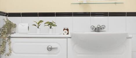 Een badkamer met een wit wastafelmeubel, een spiegel boven de wastafel en een plank met planten en toiletartikelen.