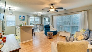 A spacious living area with a kitchen, a blue armchair, a striped sofa, and a ceiling fan. - 1 Mi to Boardwalk & Dtwn: Myrtle Beach Condo (Myrtle Beach)