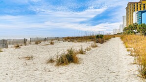 A sandy beach path with a wooden fence, leading to a building with a blue facade. - 1 Mi to Boardwalk & Dtwn: Myrtle Beach Condo (Myrtle Beach)